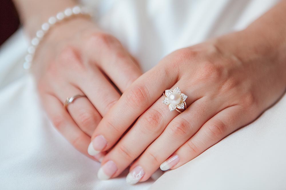 bride hand with diamond ring pearl bracelet white dress